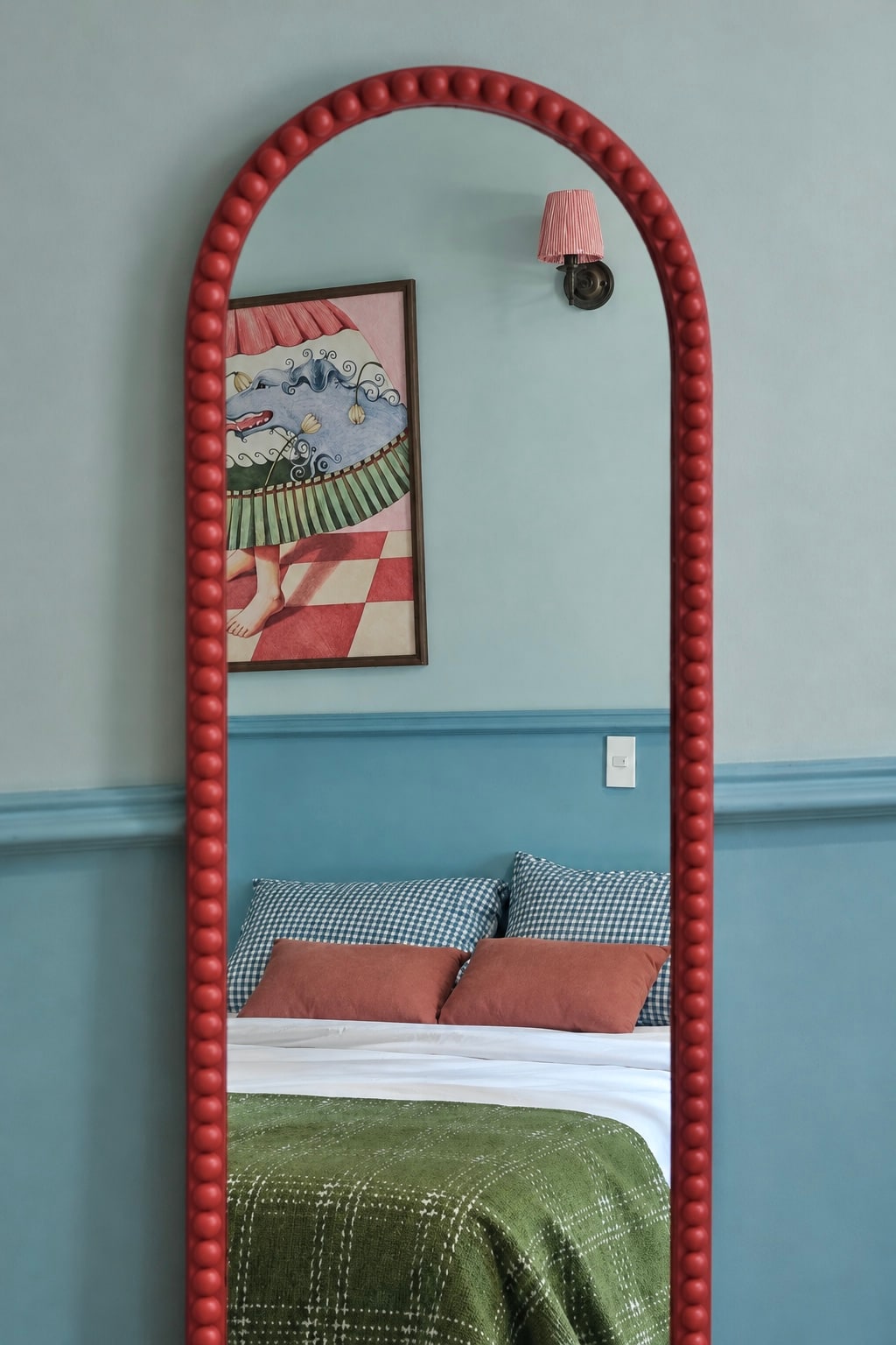 Coral-framed mirror reflecting the MARE bed, artwork and wall light